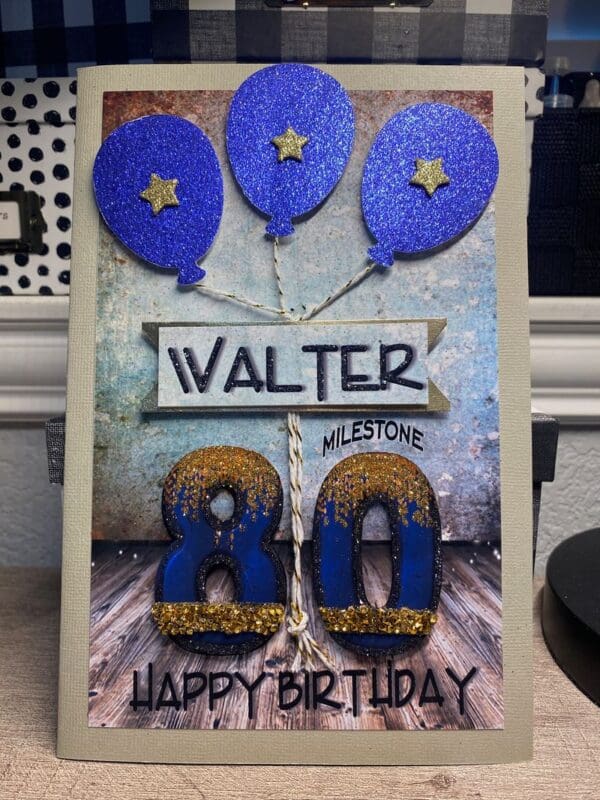 A birthday card with blue balloons and gold letters.