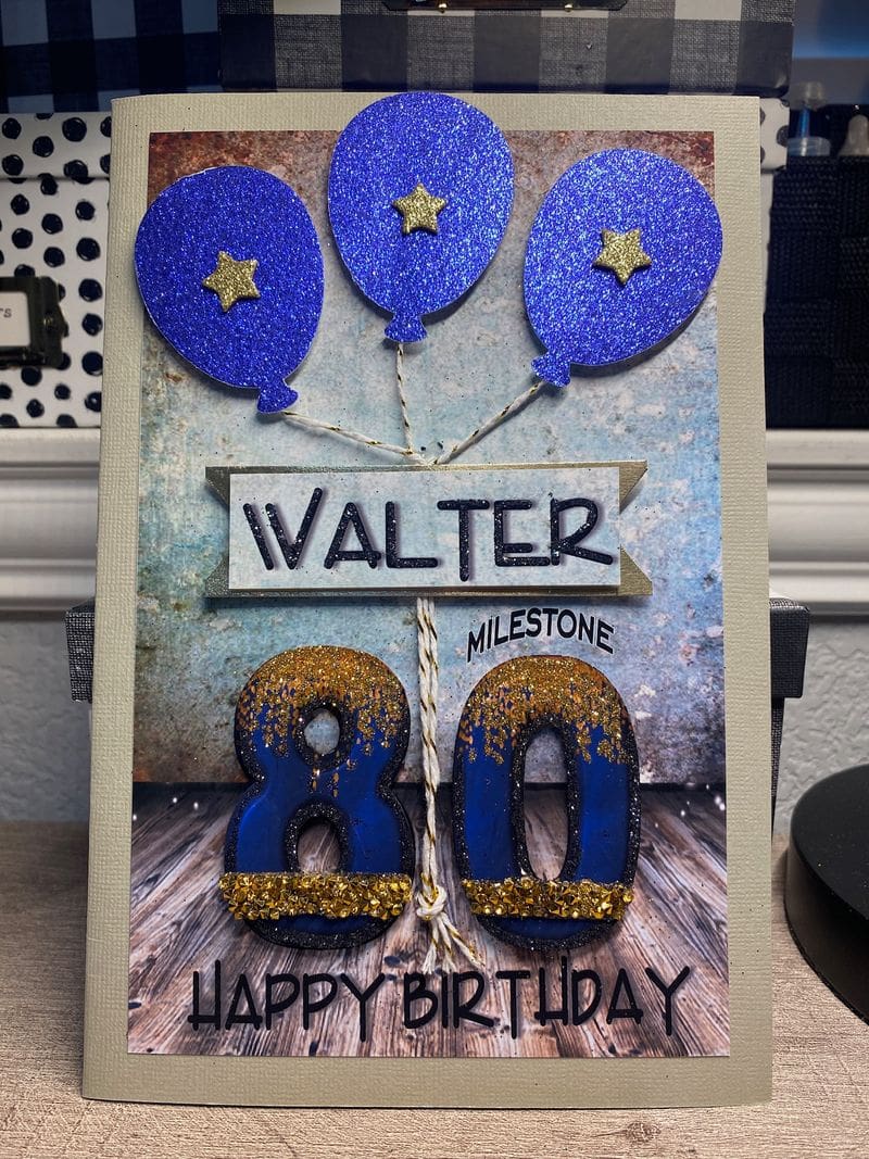 A birthday card with blue balloons and gold letters.