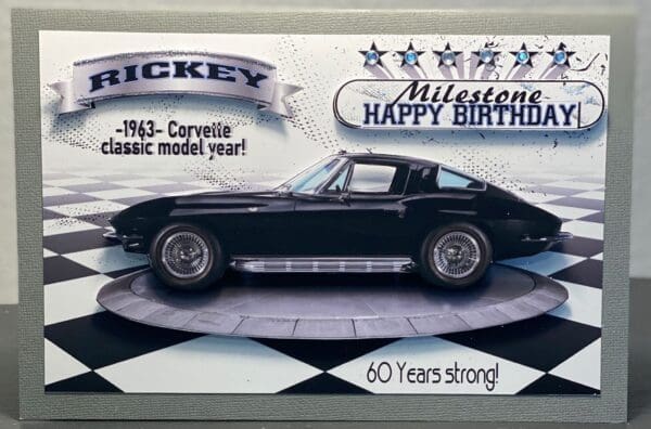 A black corvette is on display in front of the mickey mouse birthday sign.