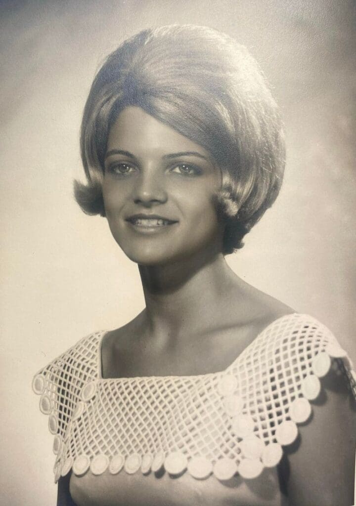 A young woman in a white dress is smiling.